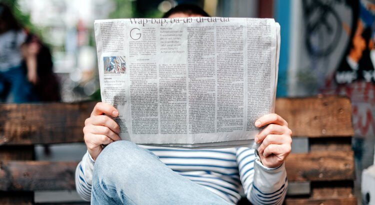 Mann sitzt auf Bank und liest Zeitung